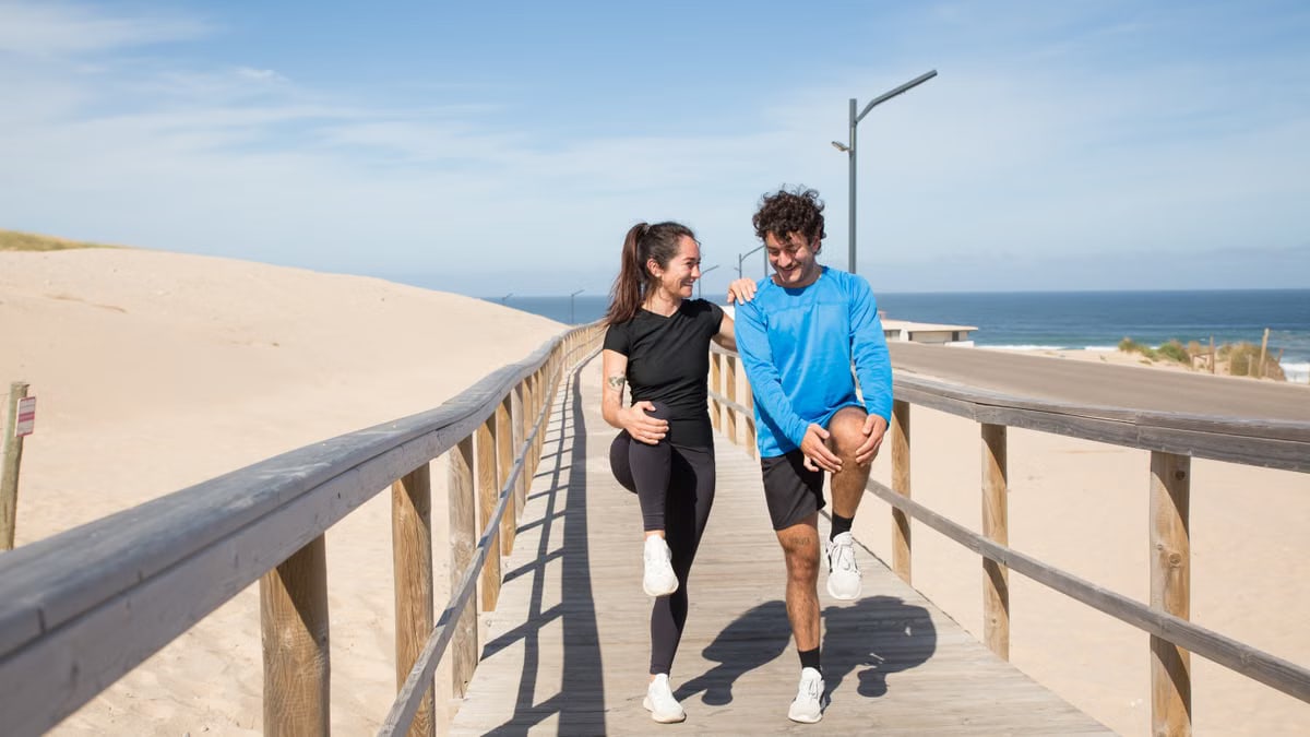 A young couple doing warm-up exercises on a boardwalk by the beach, enjoying a healthy lifestyle outdoors.